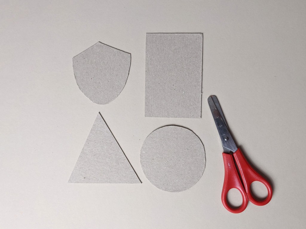 Image of a pair of safety scissors, and four shapes cut from card. Clockwise from top left: shield, rectangle, circle, triangle.